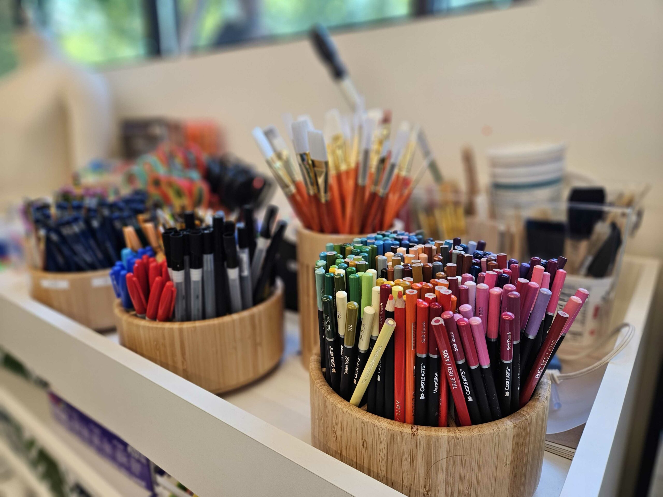 Colorful art supplies neatly organized on a tray in light wooden cups.