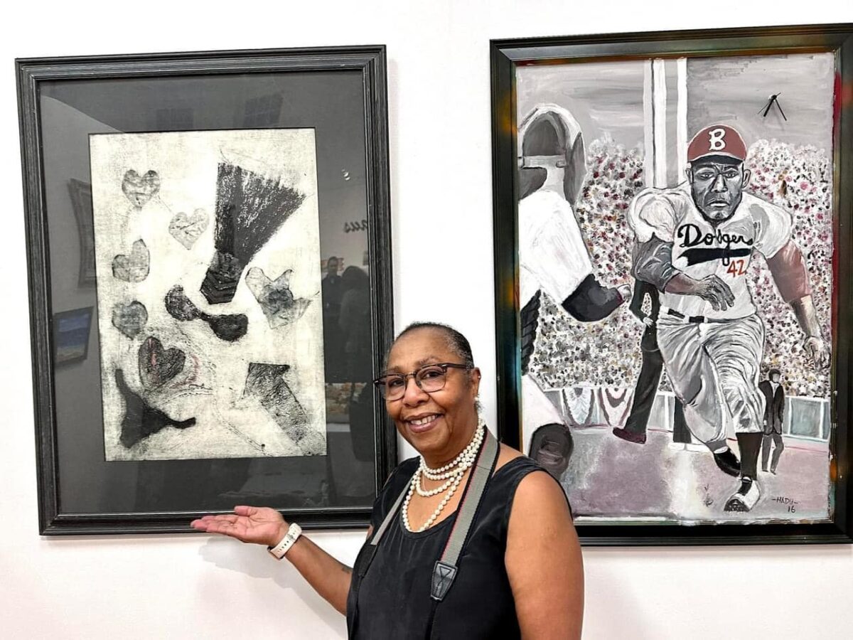 Woman smiling in front of two pieces of framed artwork on a wall.