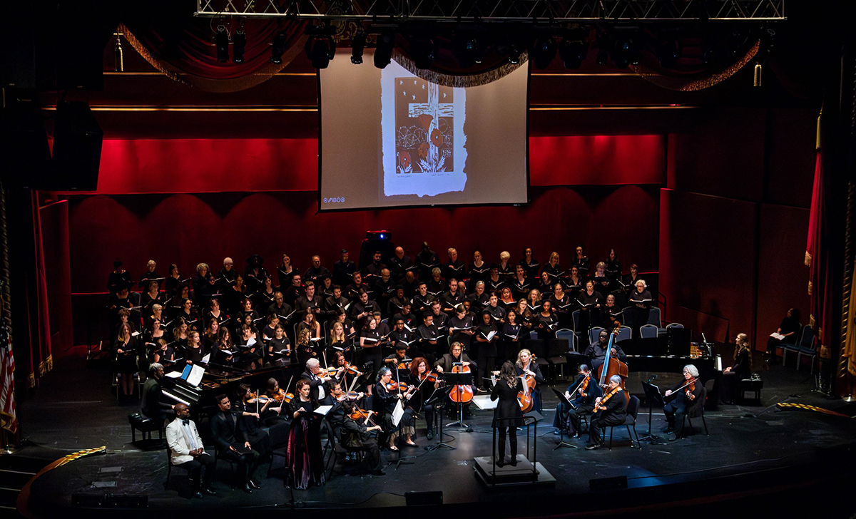 An orchestra on stage with a projection screen overhead displaying artwork.