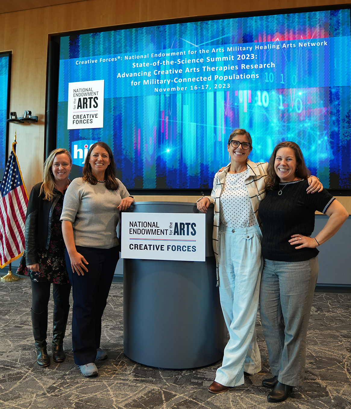 Four white women smiling while standing by a podium that has a sign that says "National Endowment for the Arts Creative Forces."