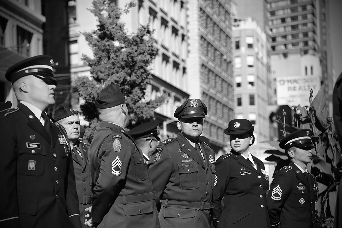 Black and white image of men and women in formal military uniforms with city buildings in the background