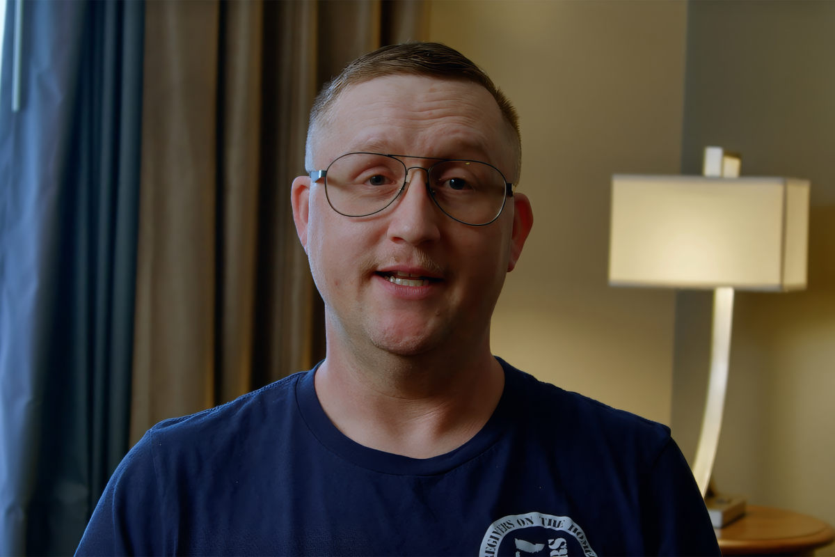 A white man with short brown hair and wire framed glasses sitting in a living room.